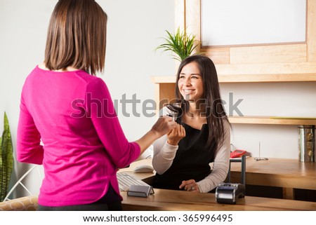 Cute young woman at the cash register taking a credit card from the hand of a customer and smiling