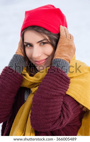 Beautiful girl outdoor in cold snowy winter, looking playful with red cap, comforter and gloves.