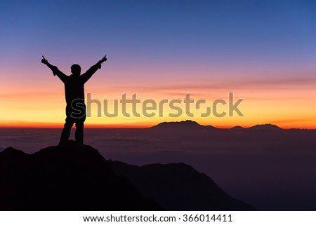 silhouette of man standing and spread hand on the top of mountain to enjoy colourful sky. Royalty-Free Stock Photo #366014411