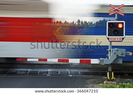 Motion blur speeding passenger train passing through a railway crossing with gates. 