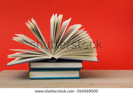 Hardback books, diary, fanned pages on wooden deck table and red background. 