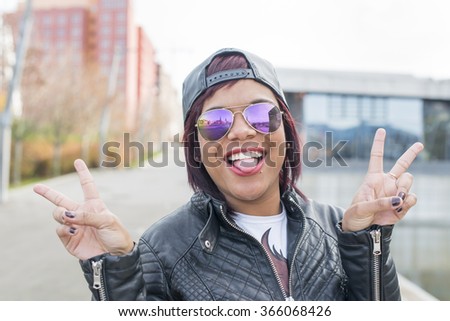 Hipster excited beautiful latin woman with sunglasses showing her tongue in the street.