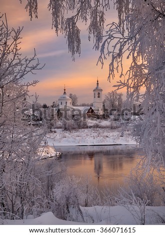 Picture of the Russian winter with a village and church on the far bank of the not frozen river in framing of trees in a hoarfrost