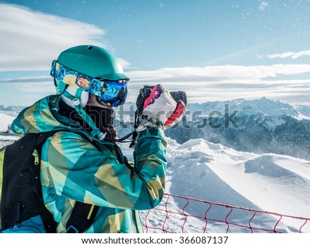 Young girl with backpack taking a photo on the top of mountains, winter sport, snowboarder