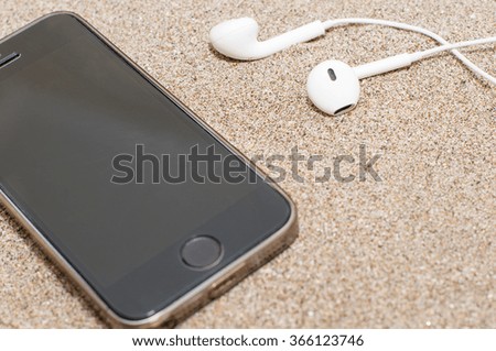 Smartphone with headphones on sea sand. Summer beach. Top view with copy space, selective focus. 