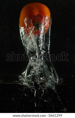 The red tomato and sparks are shined by flash at falling in water on a black background. The picture is turned 
