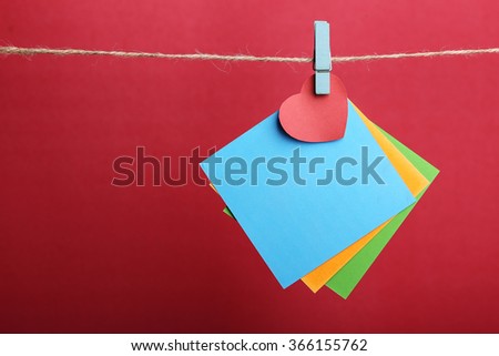Blank sticky notes with red heart hanging against red background.