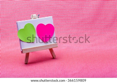 wooden easel with pink and green color heart on canvas background..