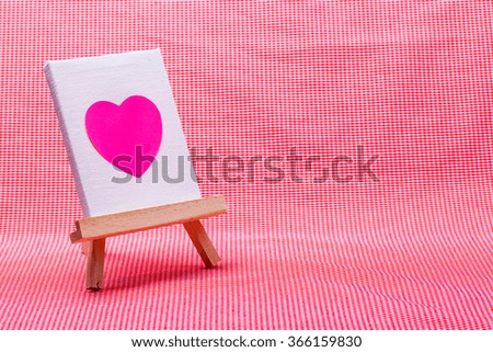 wooden easel with pink heart on canvas background..