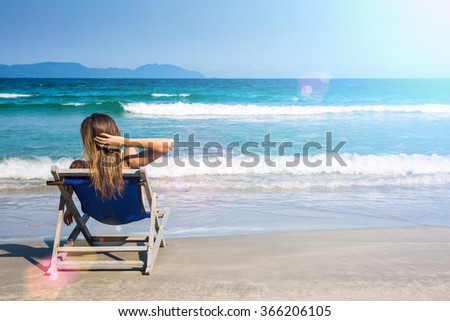 Woman relaxing on a beach chair near beautiful tropical sea, edited with sun flares. Summer vacation concept