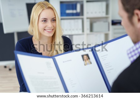 Attractive young businesswoman in a job interview with a corporate personnel manager who is reading her CV in a blue folder, over the shoulder focus to the young applicant Royalty-Free Stock Photo #366213614