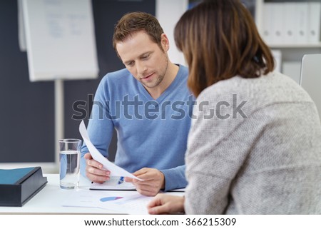 Young businessman discussing a document with a female co-worker as they share a table at the office Royalty-Free Stock Photo #366215309