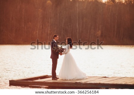 Luxury happy wedding couple kissing and embracing near lake under sunset