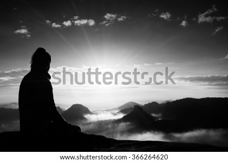 Beautiful  young woman tourist enjoy daybreak on the sharp corner of sandstone rock and watch over valley to Sun. Black and white photo