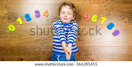 young boy playing with his collection of numbers with happy and smiling face while laying on brown wooden floor