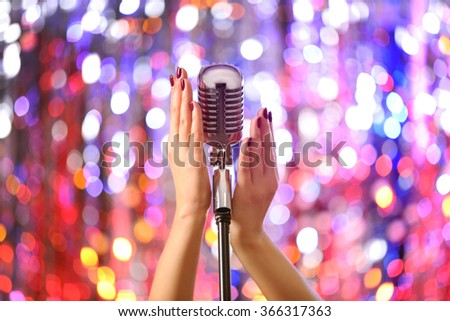 Female hands holding microphone against bright glitter background