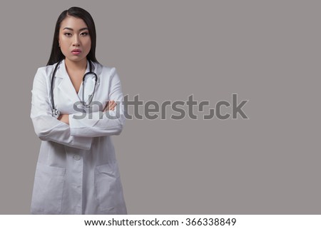 Asian woman doctor in a white coat on the isolated gray background. 
