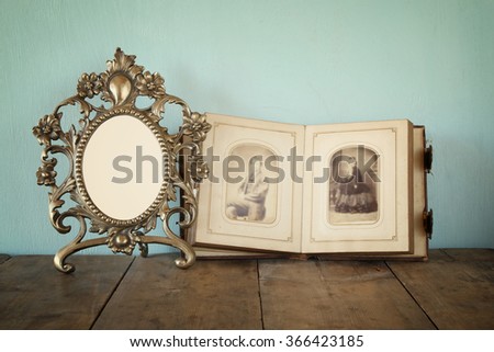 Antique blank victorian style frame and old open photograph album on wooden table. retro filtered image. template, ready to put photography
