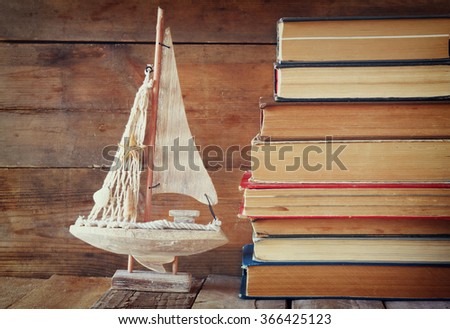 stack of old books next to decorative sailing boat wooden table. vintage filtered image
