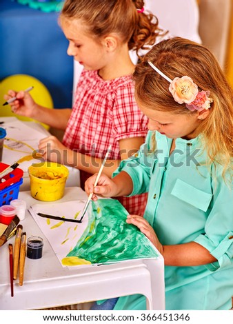 Little friendly girl painting picture on desk in kindergarten .