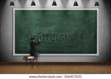 businesswoman standing on chair and drawing on blank blackboard