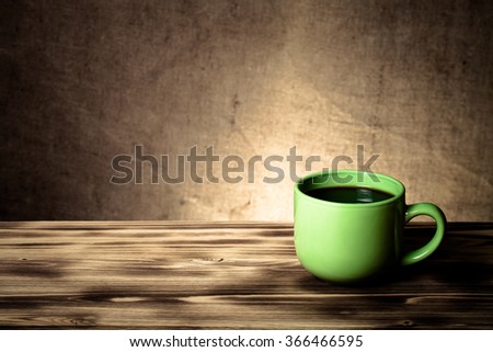 Coffee in cup on wooden table opposite a defocused burlap background. Toned.