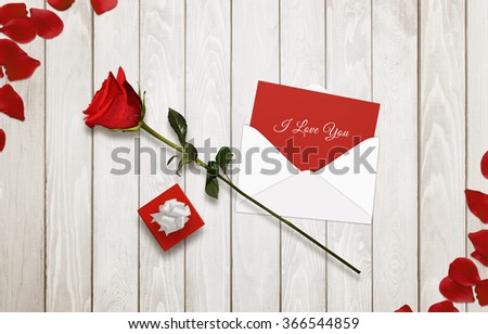 I love you message in envelope with rose and gift surrounded with petals on wooden table