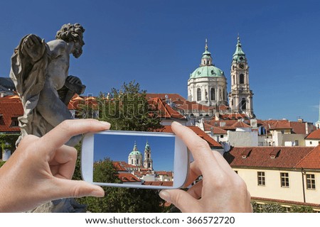 In the left bottom of the photo are hands holding smart phone and taking picture of the St Nicholas Church in Prague (Czech Republic)