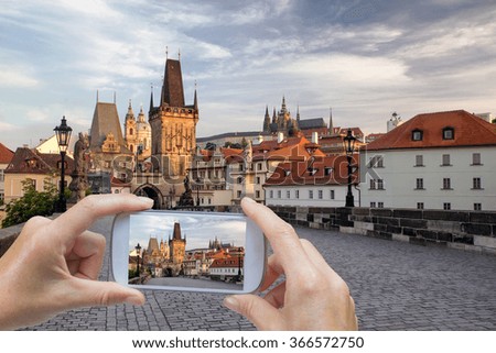 In the left bottom of the photo are hands holding smart phone and taking picture of the Charles Bridge in the early morning  (Prague, Czech Republic)