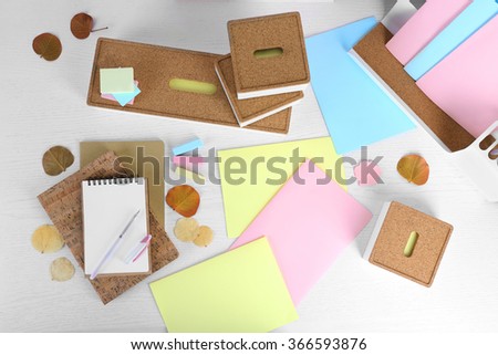 Pen with notebook, stickers, papers and dry leaves on white table