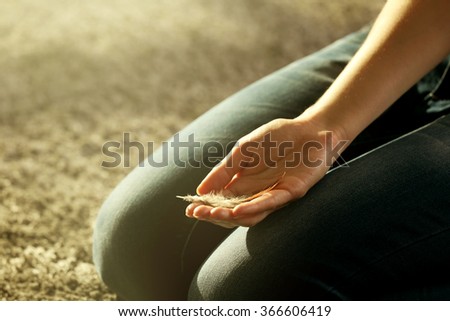 Hands holding a feather on grey carpet background, close-up