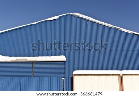 Snow on the roof of blue metal warehouse. Architectural and seasonal background.