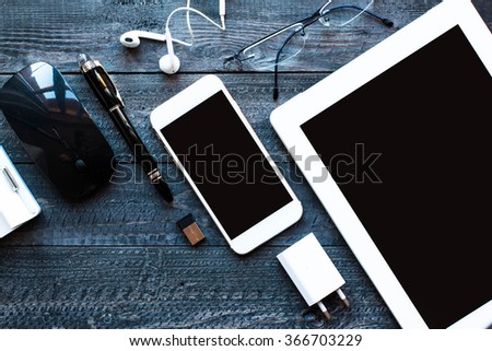 Dramatic and Dark Light Filtered Office desktop with a lot of objects including a smartphone, a tablet, a mouse, eyeglasses, a dock and more.
