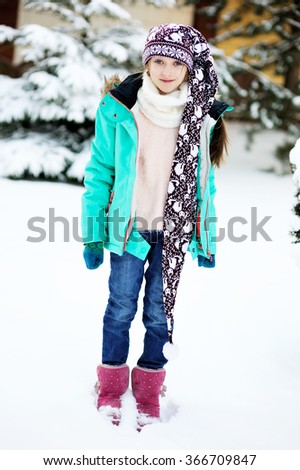 Happy adorable kid girl wearing a colorful jacket  and knitted hat playing in a beautiful snowy winter park on beauty day
