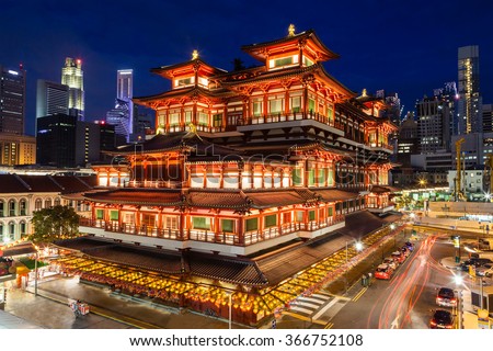 The Buddha Tooth Relic Temple comes alive at night in Singapore Chinatown, with the city skyline in the background. The temple is brightly lit in preparation for Chinese New Year. Royalty-Free Stock Photo #366752108