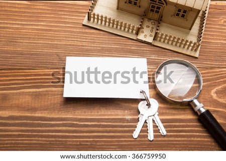 Real Estate Concept. Model house, keys, blank business card, magnifying glass on wooden table. Top view.