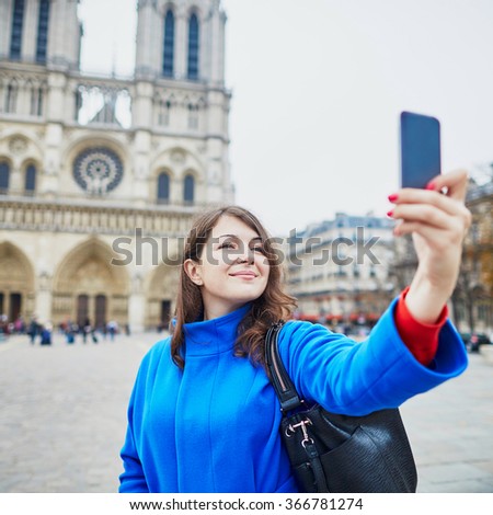 Beautiful young tourist in Paris, making funny selfie near Notre-Dame cathedral
