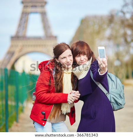 Two cheerful beautiful girls in Paris taking selfie using mobile phone near the Eiffel tower