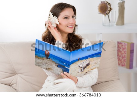 Woman with photo book is listening a seashell to bring back vacation memories.