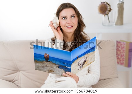 Woman with photo book is listening a seashell to bring back vacation memories.