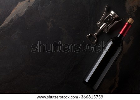 Red wine bottle and corkscrew on stone table. Top view with copy space