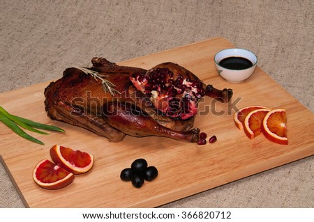Close-up photo of roasted duck served with sprig of rosemary, orange slices and pomegranate over denim background.