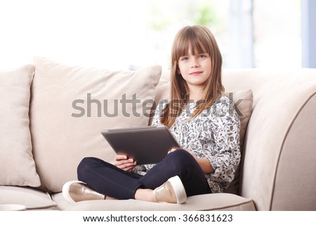 Portrait of cutie little girl using digital tablet while sitting at home in living room.