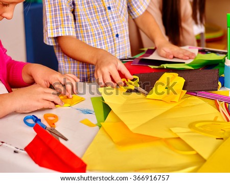 Body part of childs hands  holding colored paper on table in kindergarten .