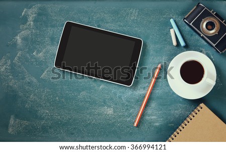 top view image of tablet, cup of coffee and photo camera over blackboard background
