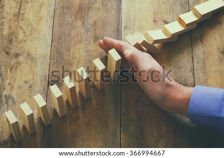 a male hand stopping the domino effect. retro style image executive and risk control concept
 Royalty-Free Stock Photo #366994667