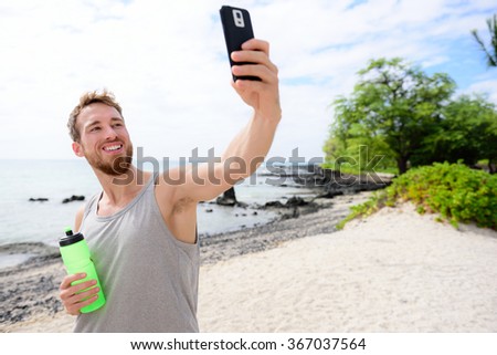 Fitness man taking selfie of himself after workout. Good looking young adult taking a self-portrait picture with his smartphone camera after exercising on a beach during summer vacation travel.