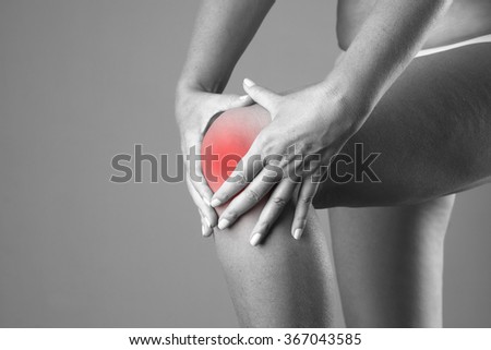 Pain in the knee. Ache in the human body on a gray background. Black and white photo with red dot