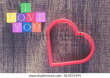 Love concept. Valentines day background with red heart and I Love You message written in colorful wooden blocks. Cross processed image with selective focus