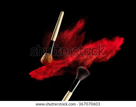 Make-up brush with red powder explosion isolated on black background